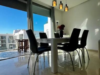 a dining table with black chairs in a living room at Luxurious 1BR Orangeraie - Terrace & Pool in Oulad Akkou