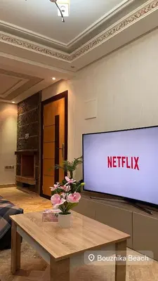 a large screen television in a living room with a table at Appartement bord de mer avec piscine à Bouznika in Bouznika