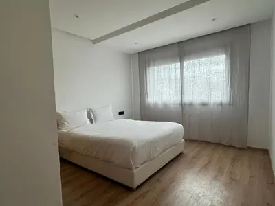 a white bedroom with a bed and a window at Appartement 1BR Prestige & Confort à Hay Riad in Rabat