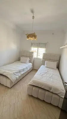 two beds in a white room with a chandelier at Appartement meublé à HARHOURA in Temara