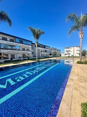a swimming pool with palm trees in front of a building at Appartement Marbella beach in Mansouria