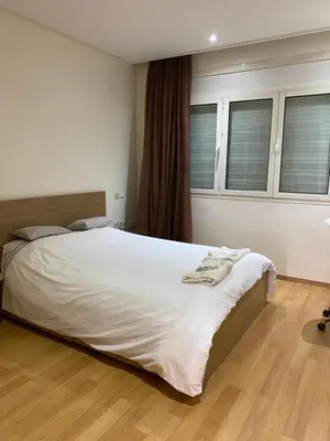 a bedroom with a bed with white sheets and windows at Joli Appartement 2 pièces in Rabat