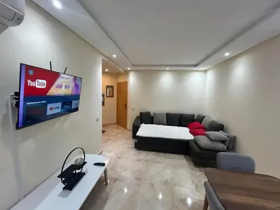 a living room with a couch and a tv on a wall at Appartement Bouznika POOL & BEACH in Bouznika