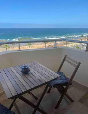 a wooden table and a chair on a balcony with the beach at Appartement vue sur mer 3 chambres in Rabat