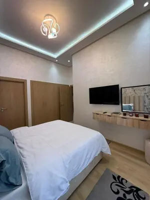 a bedroom with a white bed and a flat screen tv at Appartement 3 chambres avec piscine, proche de la plage Zenâta Eco City in Aïn Harrouda