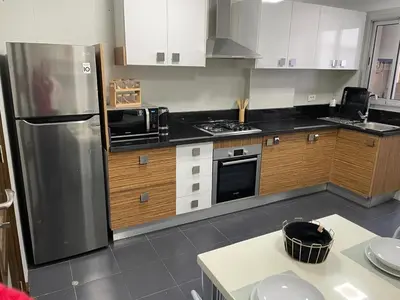 a kitchen with a stainless steel refrigerator and wooden cabinets at Magnifique Appartement familial avec piscine in Mohammedia