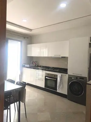 a kitchen with white cabinets and a stove and a table at Appartement en bord de Mer in Mohammedia