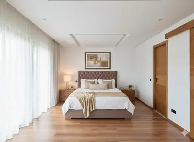 a bedroom with a large bed with white walls and wooden floors at Grande villa sécurisée piscine privée in Dar Bouazza