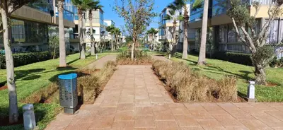 a walkway in front of a building with palm trees at Residence blue beach Sidi Rahal in Sidi Rahal