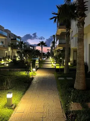 a walkway with palm trees and buildings at night at Residence blue beach Sidi Rahal in Sidi Rahal