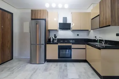 a kitchen with a stainless steel refrigerator and wooden cabinets at Piscine Chauffée Salle de Sport Balcon Panoramique in Mohammedia