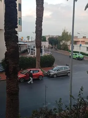 a person walking past two cars in a parking lot at Oceania in Mohammedia
