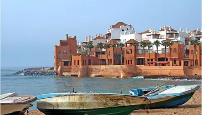 two boats sitting on the beach in front of a building at Apartment avec piscine terrasse et balcon in Bouznika