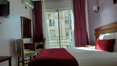 a hotel room with a bed and a desk and a window at Hôtel Amouday in Casablanca