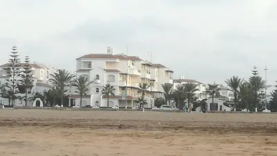 a large white building on the beach with palm trees at Garden Beach Sidi Rahal in Sidi Rahal