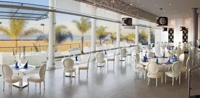 a restaurant with white tables and chairs and palm trees at Avanti Mohammedia Hotel in Mohammedia