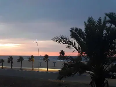 a sunset on the beach with palm trees and a street light at Appartement Casablanca Garden Beach in Casablanca