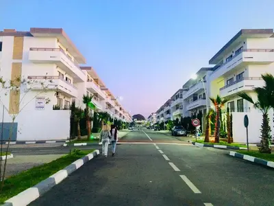 two people walking down a street with buildings at Marbella Beach location pour famille 2 chambres in Mansouria