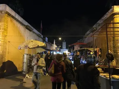 a group of people walking around a market at night at Appartement Cosy - Corniche plage Mohammedia in Mohammedia