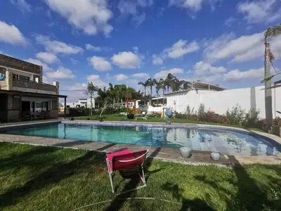 a swimming pool with a pink chair in the grass at Gîte équestre Balade plage petit déjeuner au bord de la piscine in Azemmour