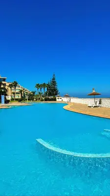 a large blue swimming pool next to a beach at Sea View Luxury Apartment Just Steps from the beach in Bouznika