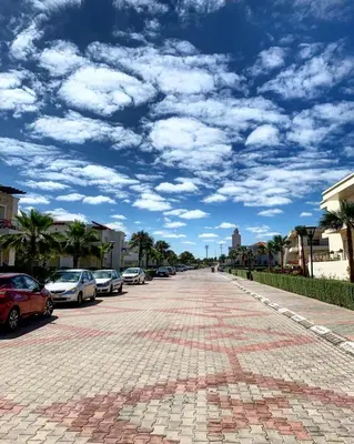 a cobblestone street with parked cars under a cloudy sky at Magnifique Appart a Savannah Beach in Sidi Rahal