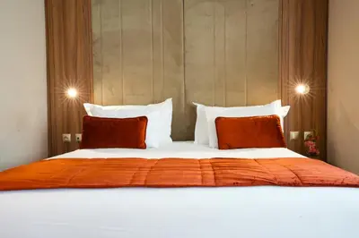 a bed with an orange blanket and two pillows at First Suites Hôtel in Rabat