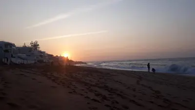 a sunset on a beach with people walking on the sand at appartement Shems Bouznika Premium in Bouznika