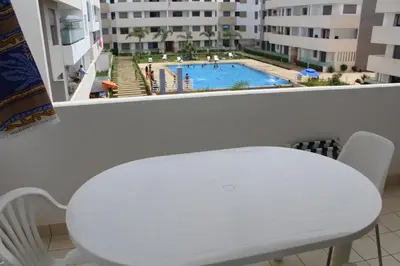 a white table and chair in a room with a view of a pool at Fermer Appartement dans résidence Paradis Beach in Mohammedia