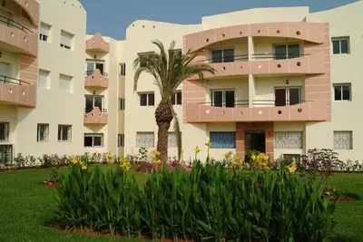 an apartment building with a palm tree and flowers at La résidence des vagues in Mohammedia