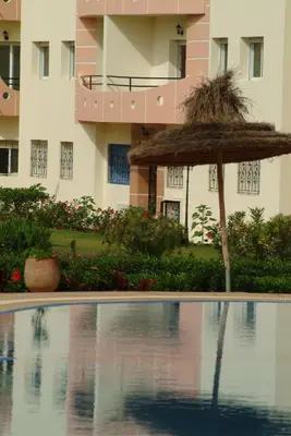 a pool with a straw umbrella and a building at Super Appartement MOHAMMEDIA in Mohammedia