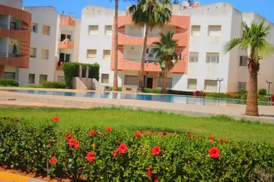 a courtyard of a building with red flowers and palm trees at MOHAMMEDIA 304 in Mohammedia