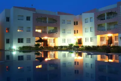 an apartment building at night with its reflection in the water at Appartement sable et soleil in Mohammedia