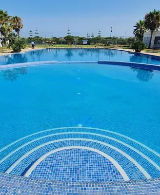 a large swimming pool with blue water at Bel appartement Savannah Beach in Sidi Rahal
