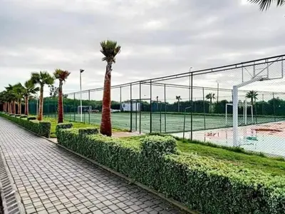 a fence with palm trees next to a tennis court at Bel appart à Hacienda Beach Sidi Rahal in Sidi Rahal