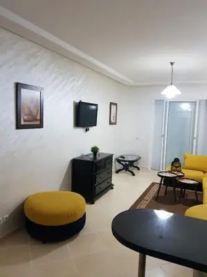a living room with a tv and a table and chairs at Sidi Rahal , Residence Garden Beach 2 in Sidi Rahal