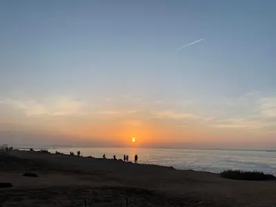 a group of people standing on a beach at sunset at Appartement de standing vue sur mer à Mohammedia in Mohammedia
