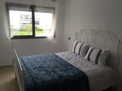 a bedroom with a bed with a blue and white bedspread and a window at Grand Apartement a Blanca Beach Sidi Rehal in Sidi Rahal