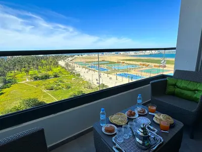 a balcony with a table with food and a view of the beach at luxe appartement met zeezicht en zwembad Mohammedia Parc in Mohammedia