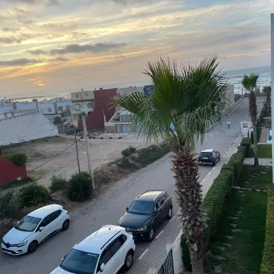a group of cars parked on a street with a palm tree at Résidence Galets Sur Mer in Dar Bouazza